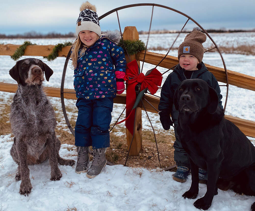 Two kids and two dogs against a fence in winter